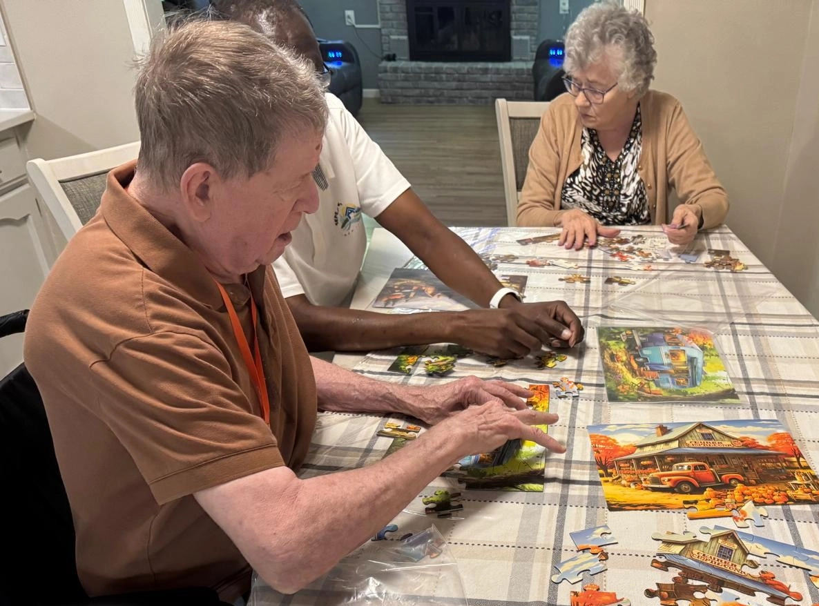Home Caregiver Assisting Senior Residents With A Puzzle Activity In A Shared Living Area