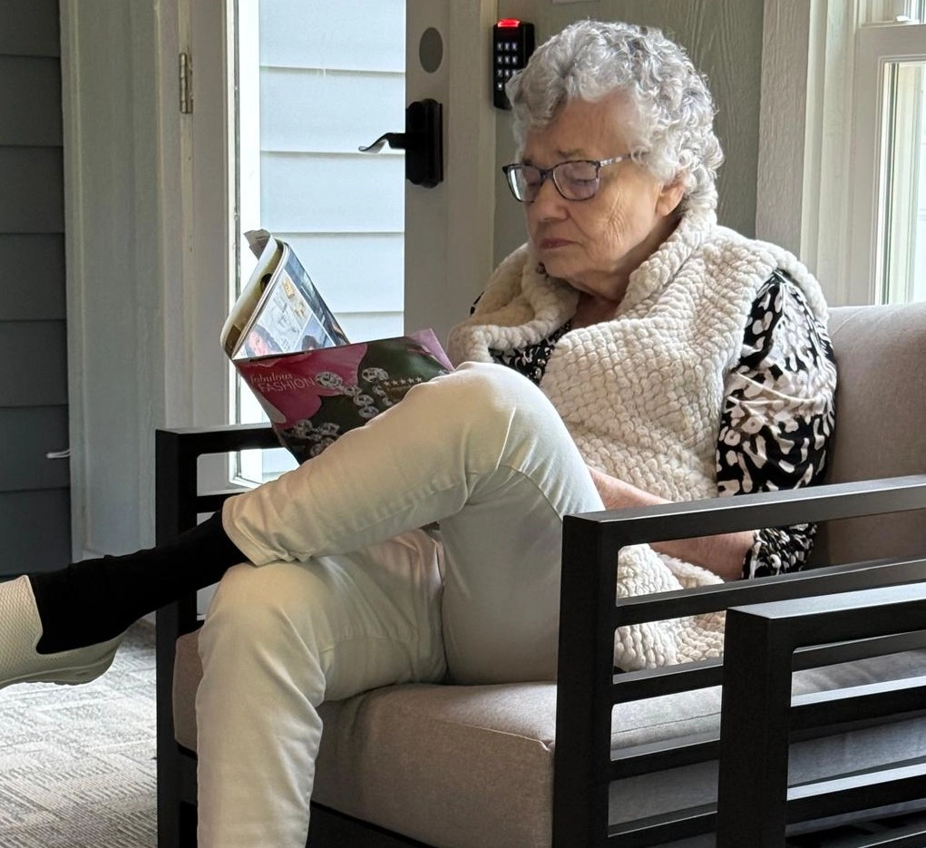 Home Senior Resident Sitting In A Chair Reading A Book In A Calm Home Environment
