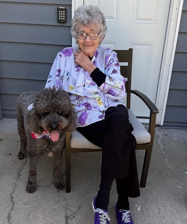 Senior Resident Sitting On A Patio Smiling With A Dog In A Calm Outdoor Setting