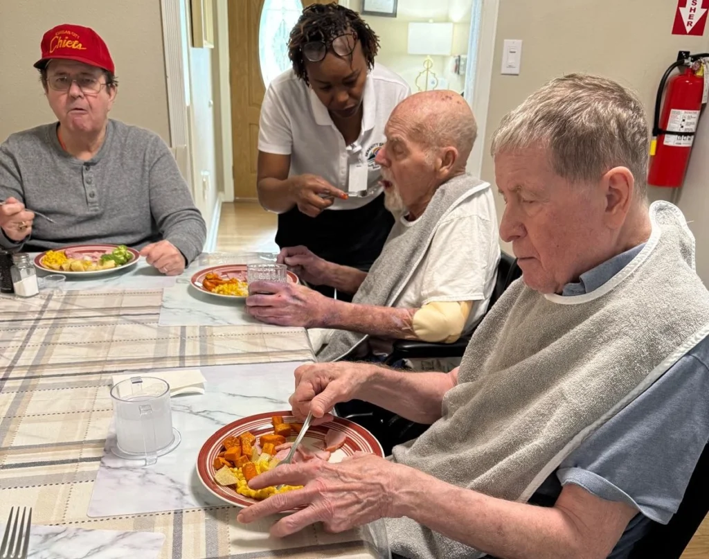Senior Residents And Caregiver Enjoying Dinner Together In A Warm Supportive Environment 1024x807