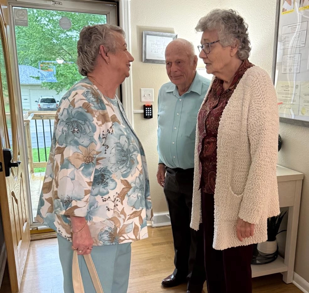 About Three Elderly Residents Having A Friendly Conversation In A Care Facility Hallway