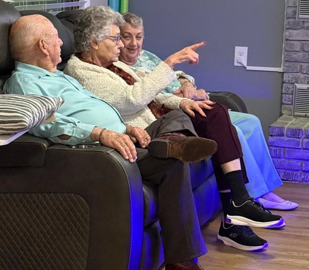 Three Elderly Residents Sitting On A Couch Having A Friendly Conversation In A Home Care Setting 1024x896