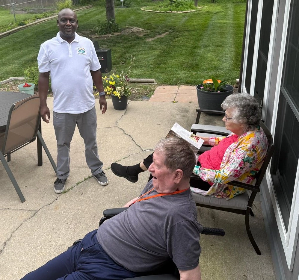 Two Senior Residents And A Caregiver Relaxing Together On A Patio